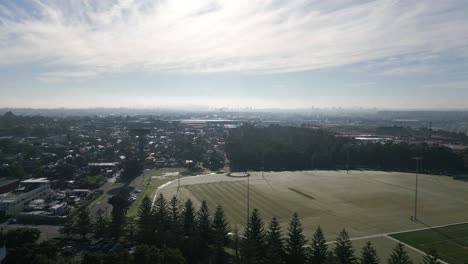 sobrevuelo aéreo de viviendas residenciales de barrio, parque y campo deportivo con el horizonte de sydney en silueta