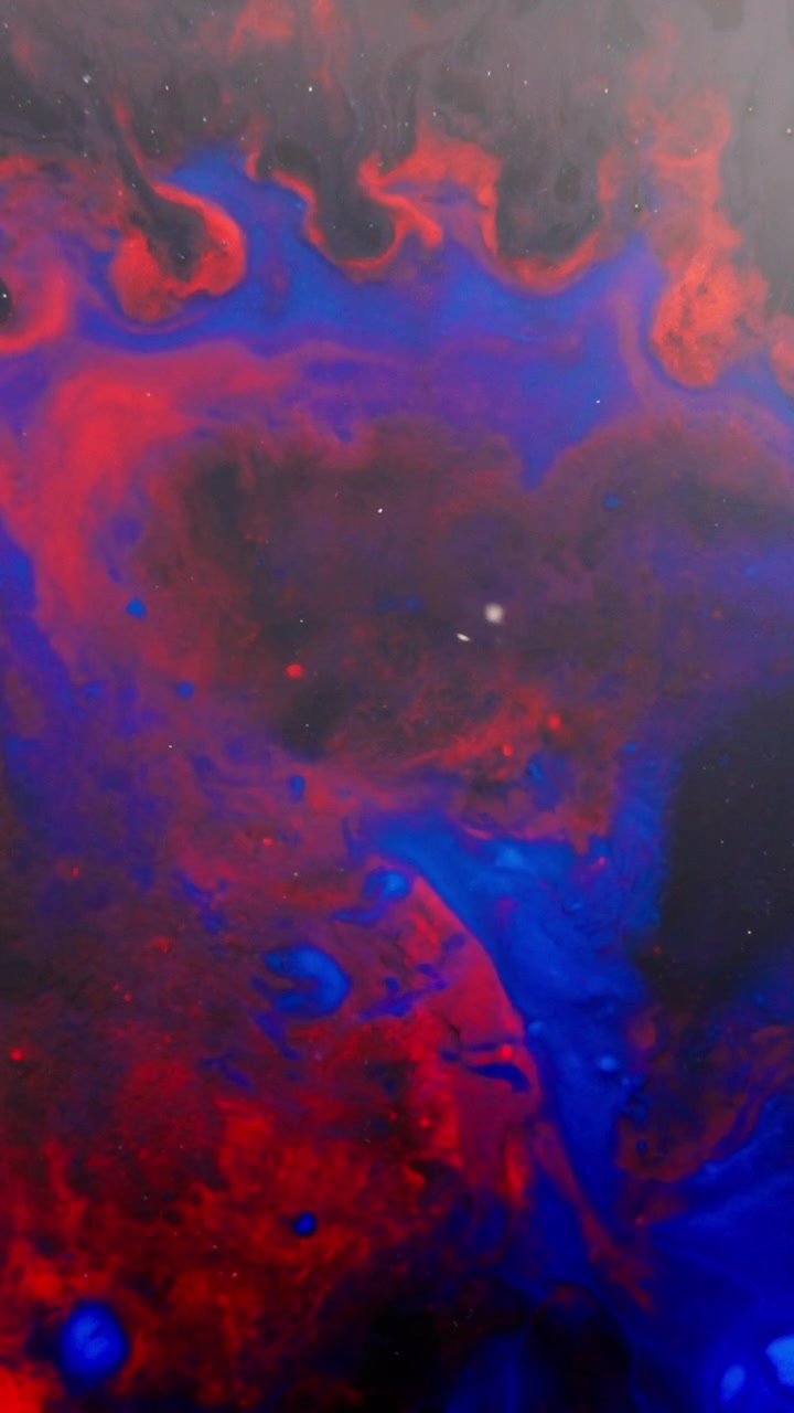 Motivi di inchiostro rosso e blu vorticosi si fondono in un liquido scuro, creando forme astratte cosmiche.