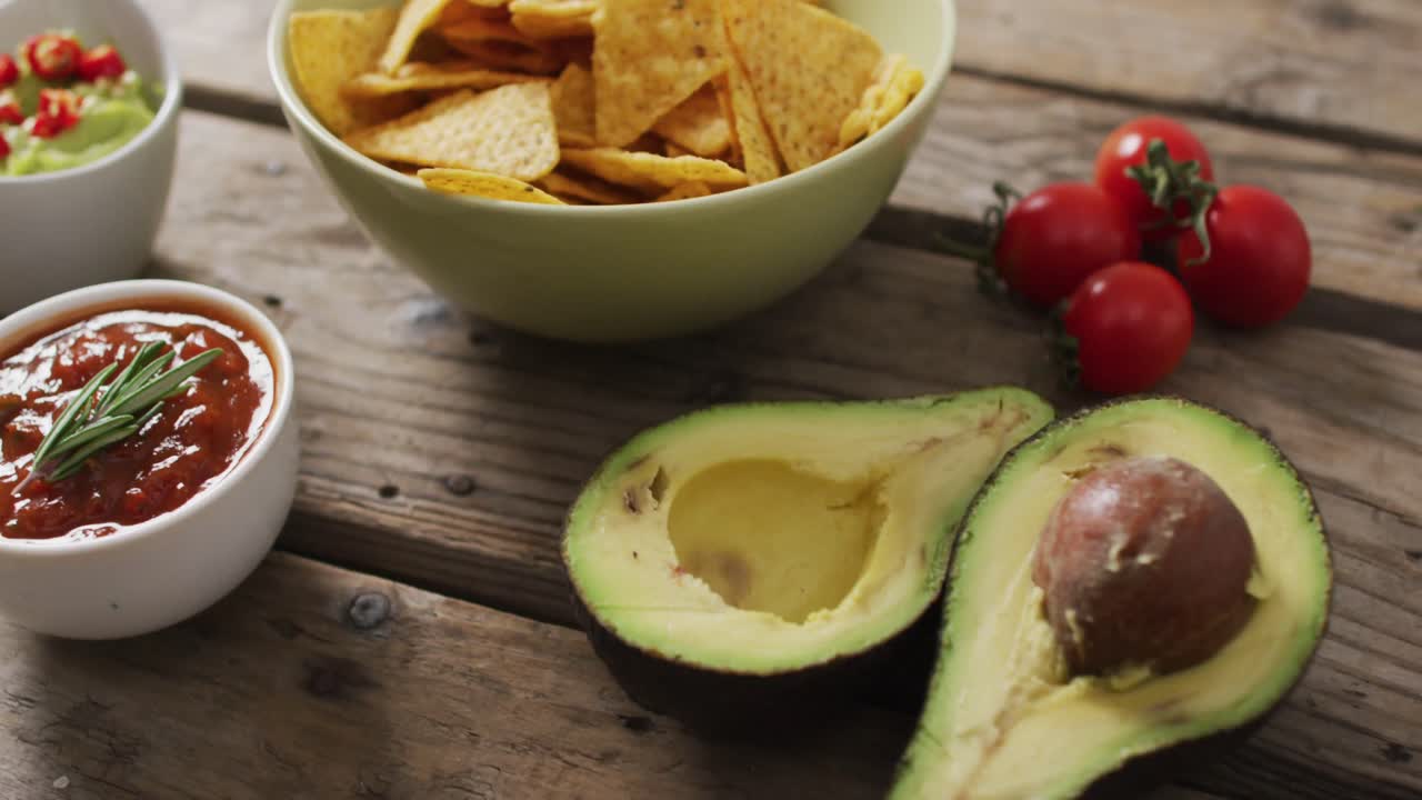 acercamiento de papas fritas en un tazón, salsas y aguacate en superficie de madera