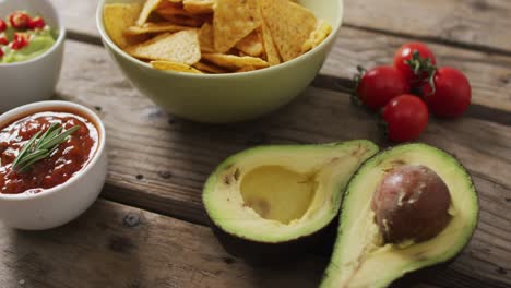 Close-up-of-potato-chips-in-a-bowl,-sauces-and-avocado-on-wooden-surface
