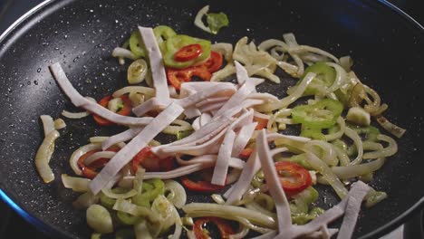 A-close-up-looking-into-a-skillet-of-oiled-sliced-onions-with-peppers-and-then-thin-strips-of-ham-are-added-and-mixed-around-the-pan-with-a-wooden-spatula