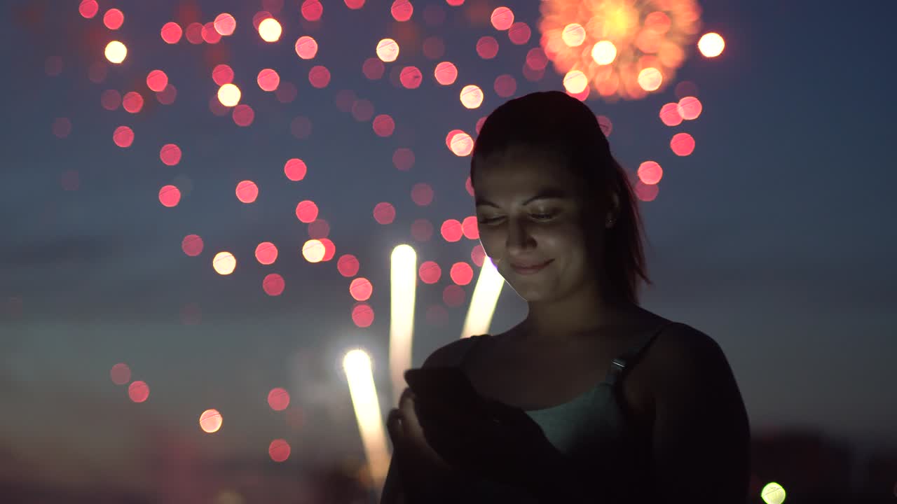 una chica usa un teléfono inteligente durante un fuego artificial. 4k