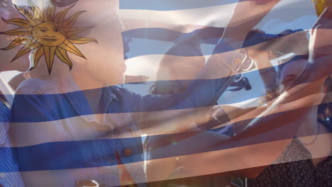 composite video of waving uruguay flag over group of diverse friends toasting beers in the car