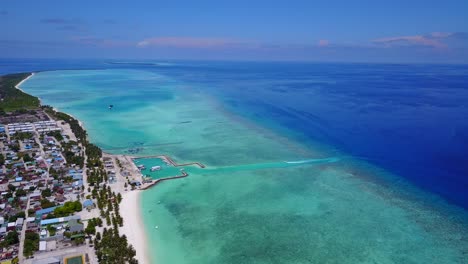 vista aérea a gran altura de una isla cubierta de palmeras en las maldivas mientras el color del mar va de turquesa a azul oscuro