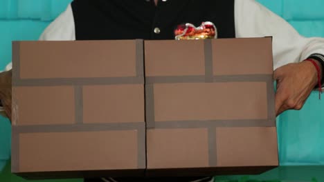 person holding two cardboard cubes with brick-like patterns against a teal background