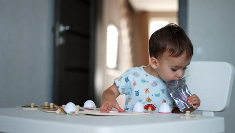 toddler boy sitting at the desk with the toys. kid drinking juice from the pack. blurred backdrop.