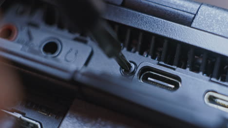 camera repair person using a small screw driver to loosen a tiny screw on the side of a gray professional camera