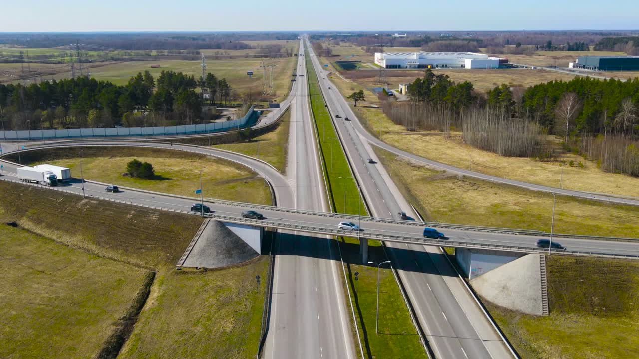 Aerial drone hyperlapse or timelapse spinning and orbiting around a large bridge intersection where cars, vehicles, buses and trucks drive on a sunny road called Tallinn Pärnu highway, green grass.