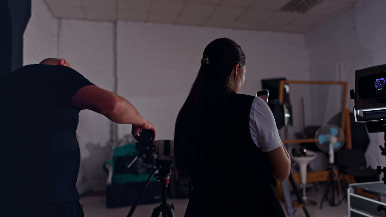 Woman taking video on her phone and man uses a professional camera. Blog video creation in studio.