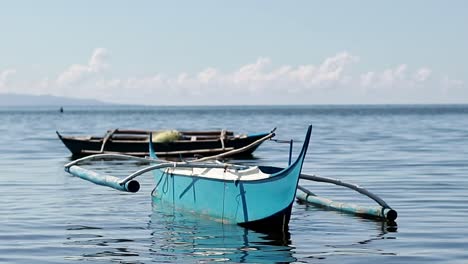 ambient motion of two traditional fishing outrigger boats or bangka from the philippines floating on calm sea waters under a blue summer sky