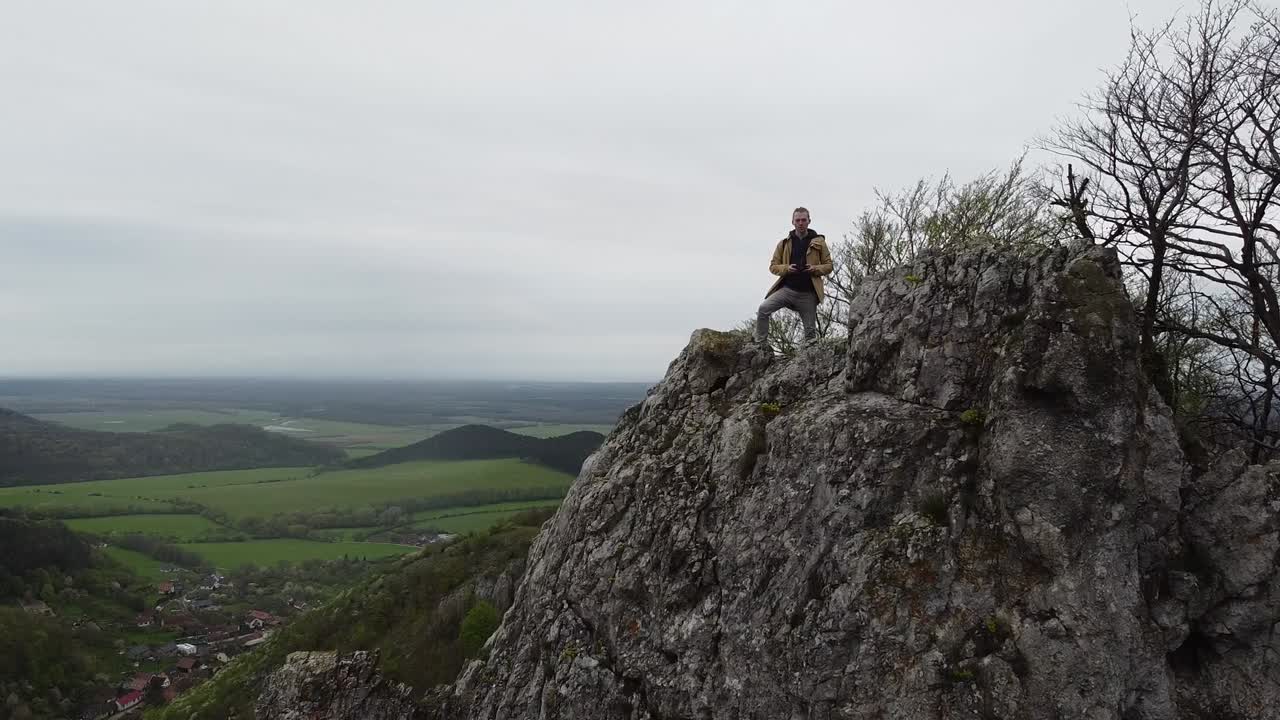 revelando viajero con mochila alcanzando la cima de un acantilado de montaña afilado colinas del bosque de color plano que muestran una pequeña aldea europea en el valle