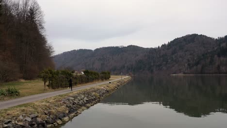 A-drone-shot-of-an-autumn-landscape-shows-a-young-man-in-a-black-tracksuit-running-along-a-path,-with-colorful-trees-covering-hills-in-the-background