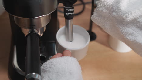 woman whips milk with coffee machine device closeup. lady in terry bathrobe prepares cream for cappuccino in kitchen. modern appliance for home cooking