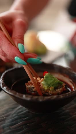 mujer comiendo un rollo de sushi tempura con palillos