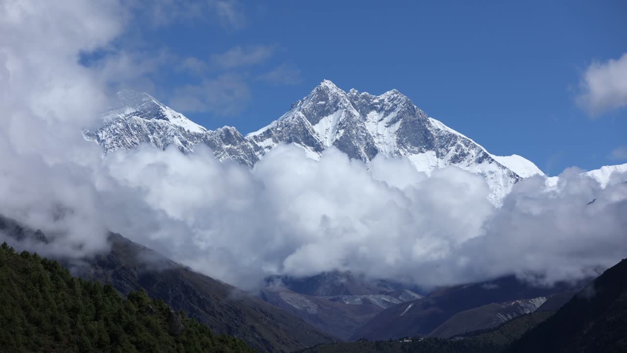 Magnificent view of the Kanchenjunga Region in Nepal, with snow-covered Himalayan peaks emerging through drifting clouds, framed by lush valleys and a clear blue sky, evoking awe and tranquility