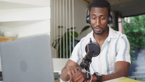 happy african american man sitting at table in kitchen, using laptop and making vlog