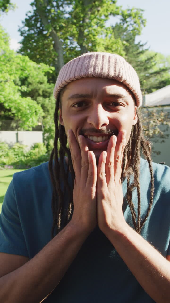 Video verticale di un uomo birazziale sorridente con dreadlocks e un cappello che sorride alla telecamera.