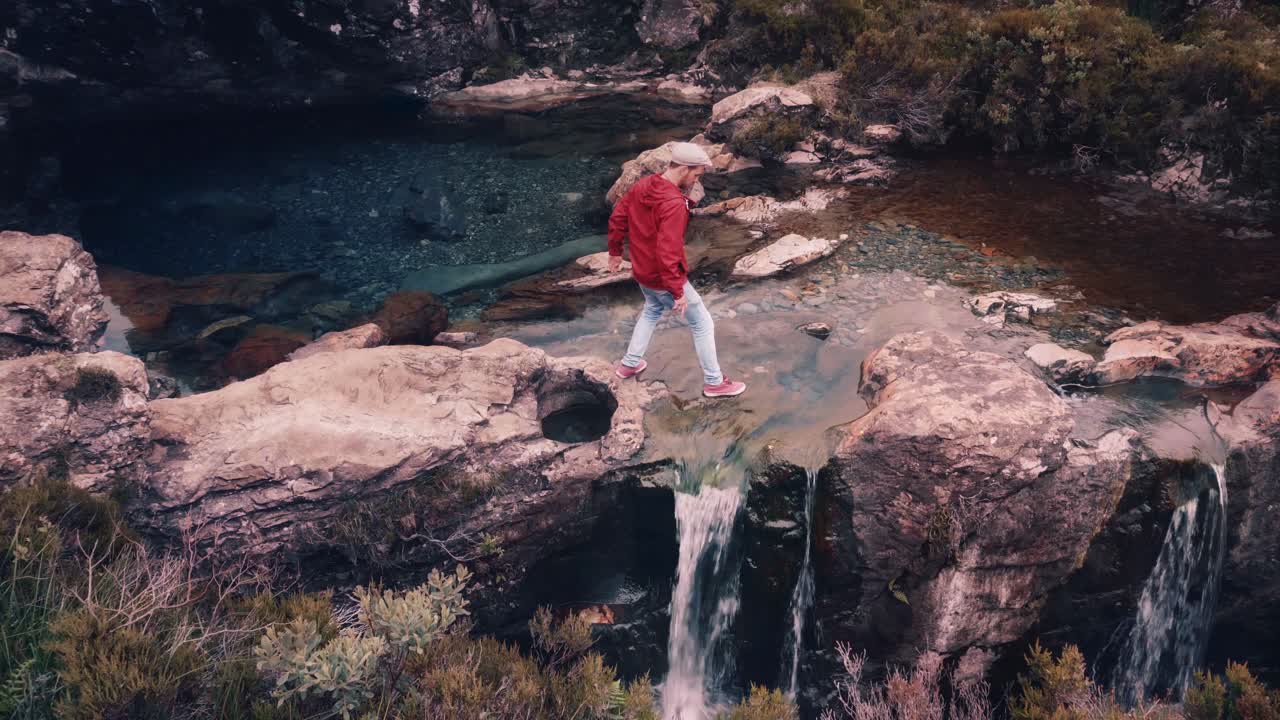 Cinemagraph of young man in red jacket walking at Fairy Pools, Isle of Skye with waterfalls flowing