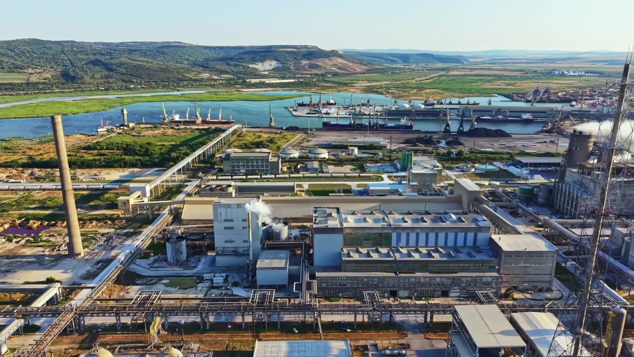 Zona industrial con fábricas, barcos y paisaje durante el día sobre un río en una región costera.