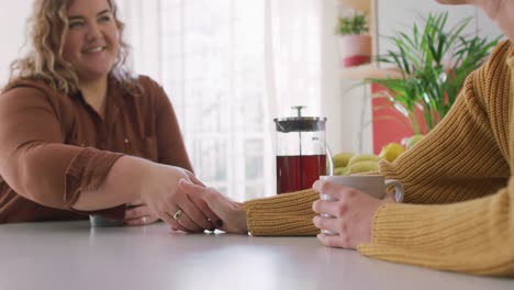 lesbianas caucásicas felices bebiendo café y tomándose de las manos en la cocina