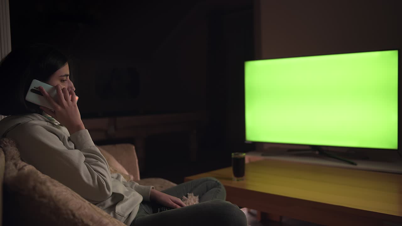 Una ragazza siede da sola a casa la sera parlando al telefono cellulare, chromakey