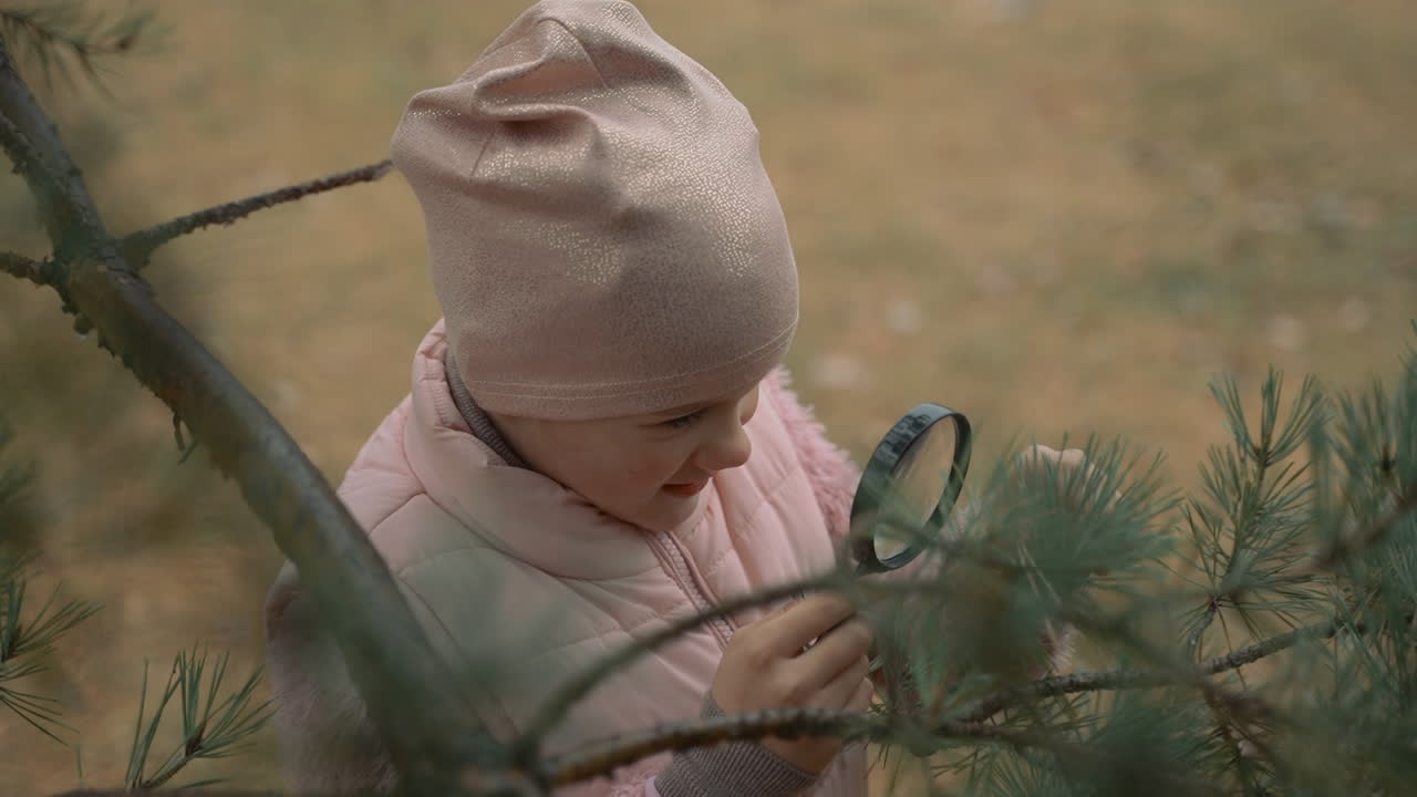 작은 소녀가 숲에서  ⁇ 보기 안경을 통해 식물을 보고 있습니다. 클로즈업. 자연과 과학에 관심이있는 아이.