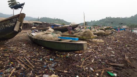 Holzboot-Am-Strand-Liegend-Mit-Einem-Fischer,-Der-Sein-Fischernetz-Reinigt