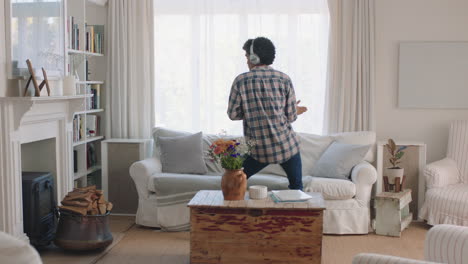 happy young man dancing at home celebrating success listening to music wearing headphones having fun dance in living room on weekend