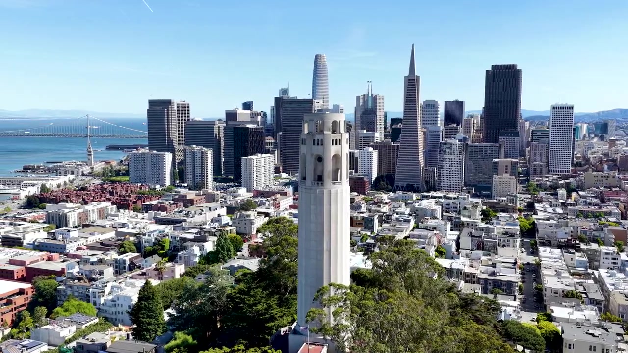 Droneoptagelser, der cirkler om Coit Tower med skyskrabere fra downtown San Francisco og havnefronten i syne