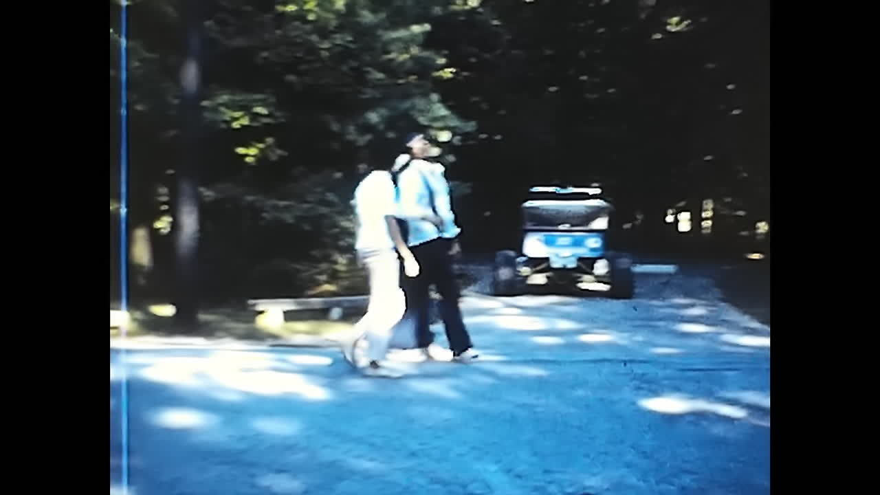 Classic Blue Car Driving on Road by Lush Green Hillside. CIRCA USA - 1970s: A vintage blue car cruises along a road that runs parallel to a vibrant, verdant hillside.