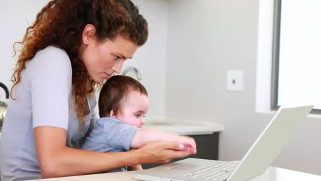 Madre-Sentada-Con-El-Bebé-En-El-Regazo-Usando-La-Computadora-Portátil