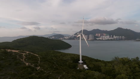 aerial approaching shot of wind turbine on green hill producing green energy on lamma island, hong kong