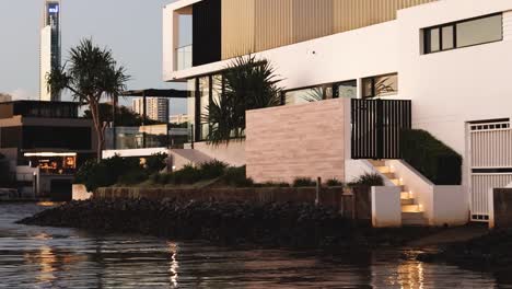 a serene view of modern riverside homes with lush greenery and reflective waters during sunset.