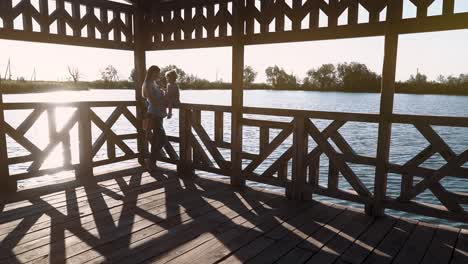 young beautiful mother sitting in a wooden structure against the sunset near the lake