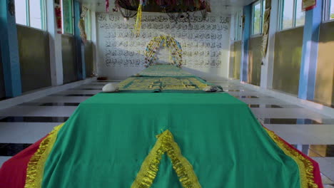 quetta, pakistan, a longest beautiful tomb in an islamic shrine, decorated and covered with green holy cloth, the arabic hundred names of god written over the back wall of tomb, tilting down view