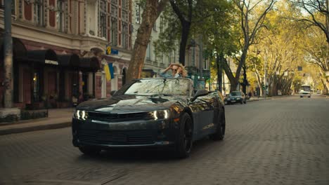 a happy blonde girl rides in the back seat of a gray cabriolet. the girl looks out of it and has fun