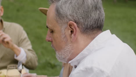 man cutting a meat fillet from a plate with vegetables and potatoes during an outdoor party in the park