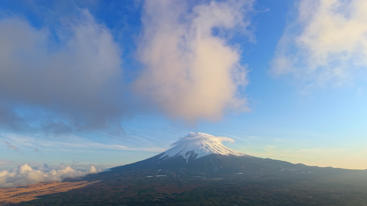 Aerial drone view of Mount Fuji with snow at the top and clouds moving around in daylight