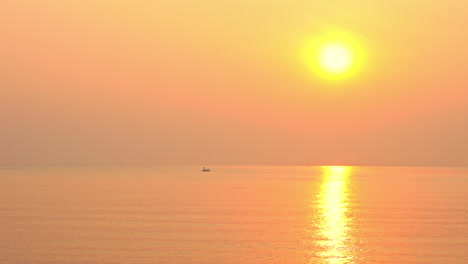 오렌지색, 분홍색, 노란색 일몰의 바다에 작은 배가 떠 있다