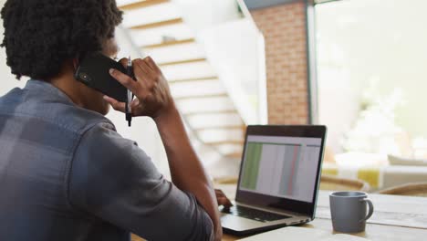 African-american-man-working-from-home-and-using-laptop-and-smartphone