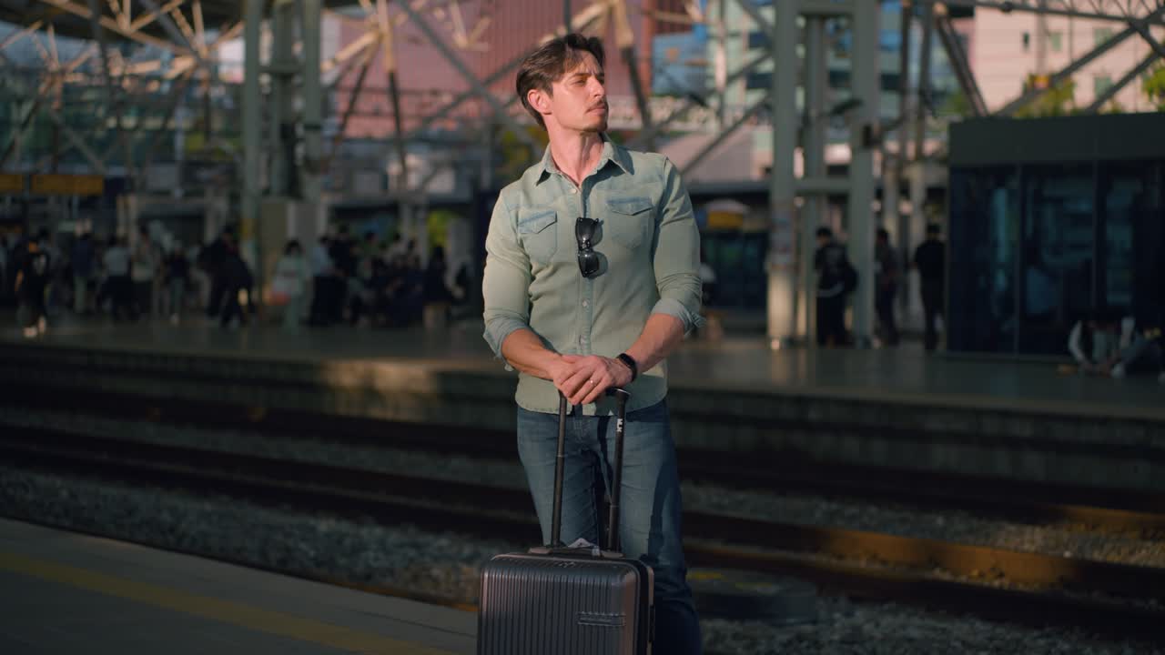 Traveler Waiting Train. Handsome man standing and shuffling side to side resting arms on suitcase luggage at Seoul train station, South Korea, stylish solo traveler in urban setting, orbit