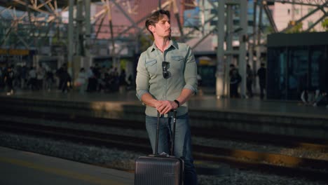 traveler waiting train. handsome man standing and shuffling side to side resting arms on suitcase luggage at seoul train station, south korea, stylish solo traveler in urban setting, orbit