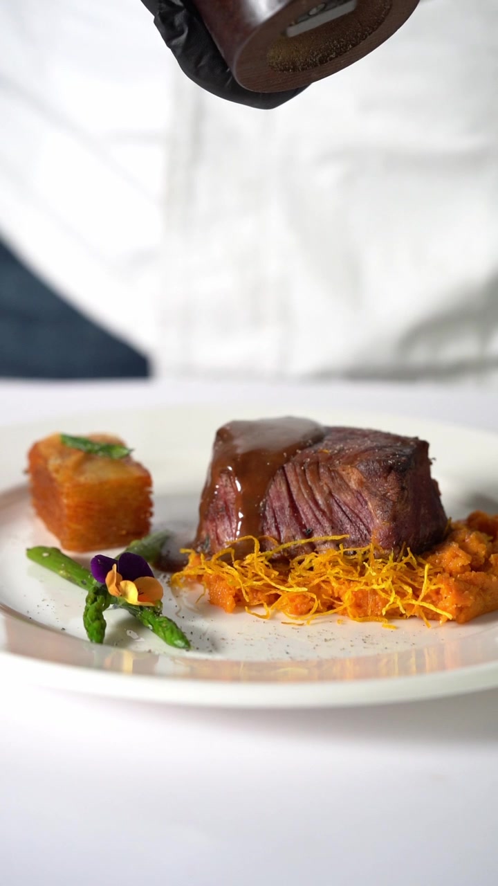 A chief plating Juicy grilled beef steak served on creamy mashed vegetables in a minimalist plate, close up shot, insert shot