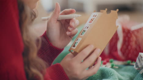 woman drawing outline on cardboard house during christmas at home