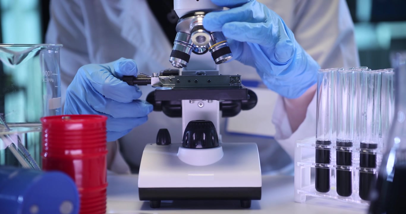 Scientist looks at specimen structure in microscope on lab desk