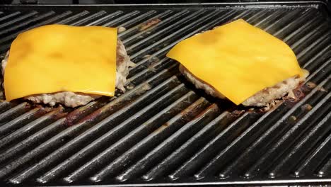 two-homemade-cheeseburgers-cooking-on-a-black-grill