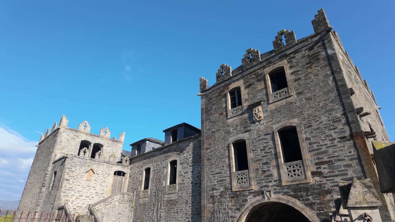 Stenfassade og tårne på Arnado-slottet i Vilamartin de Valdeorras under en blå himmel