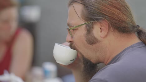 un hombre de barba de pelo largo con gafas bebe café