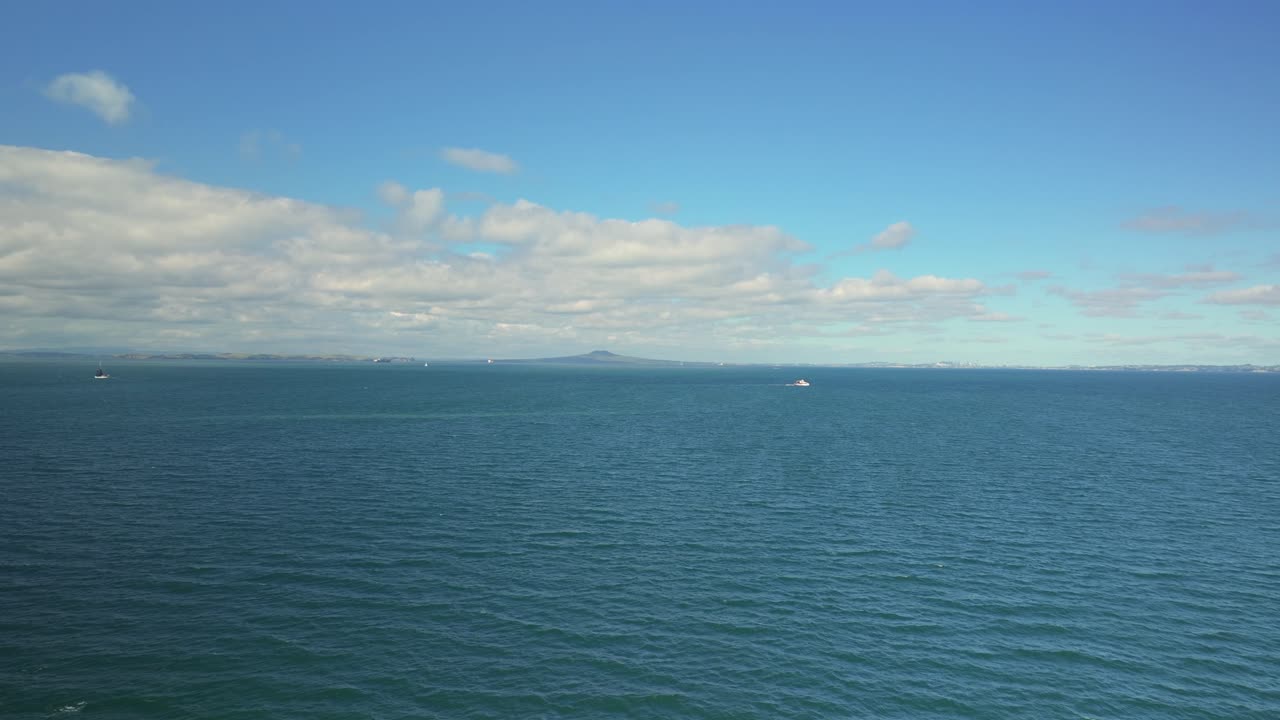 Vista drone del mare con l'isola di Rangitoto in lontananza e piccole barche che navigano sotto un cielo sereno.