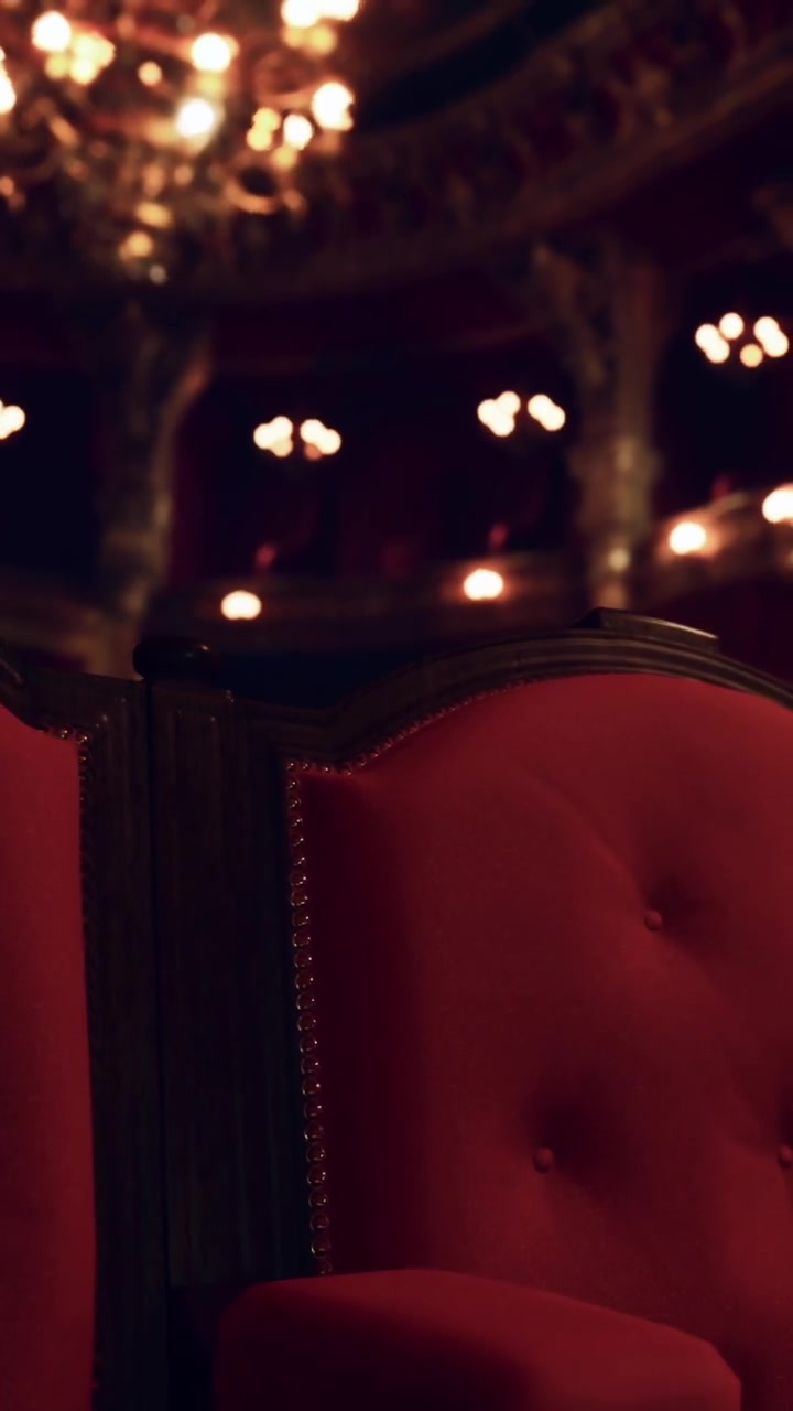Poltrona rossa in un teatro con luci sullo sfondo durante uno spettacolo.